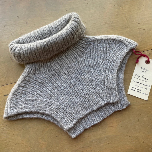 Gray turtleneck “Berlin Cowl” lying on a wooden surface.