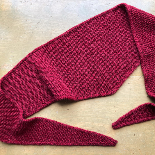 Red triangular garter stitch “Sophie Shawl” lying on a wooden table.
