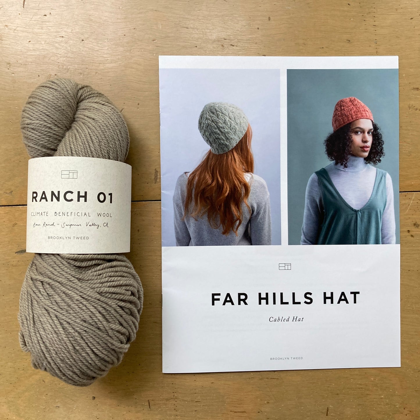One skein of Brooklyn Tweed Ranch 01 yarn and a print copy of a hat pattern lie on a wooden surface.