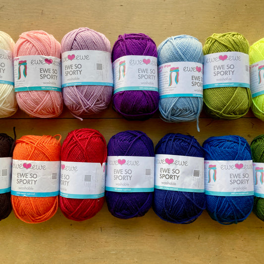 Colorful balls of Ewe So Sporty yarn lined up in two rows on a wooden surface.
