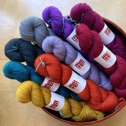 Colorful skeins of Neighborhood Fiber Co. Capital Luxury Sport in a basket on a wooden surface.