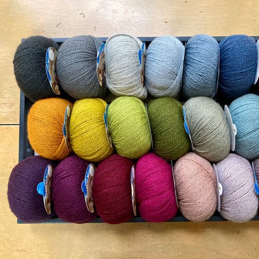 Many colored balls of Pascuali Balayage yarn arranged in a rectangular tray on a wooden surface.