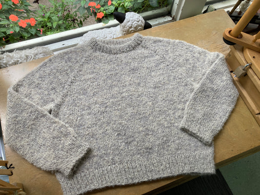 Fuzzy beige raglan pullover sweater lying on a wooden table in front of a window.