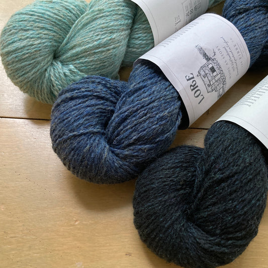 Three shades of blue Fibre Co. Lore yarn on a wooden surface.