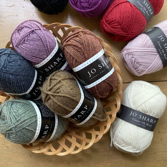 Colorful balls of Jo Sharp Classic Wool DK yarn in a basket on a wooden surface.