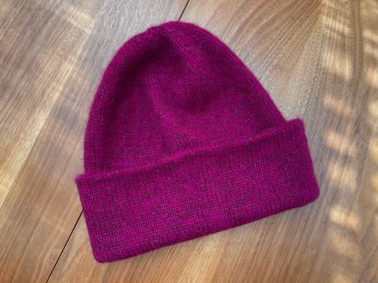 Fuzzy magenta brimmed handknit hat on a wooden surface.