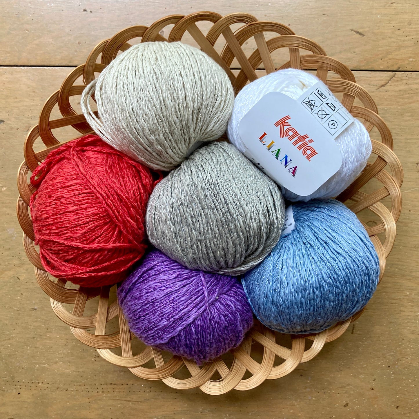 Round basket filled with colorful balls of Katia Liana yarn on a wooden surface.