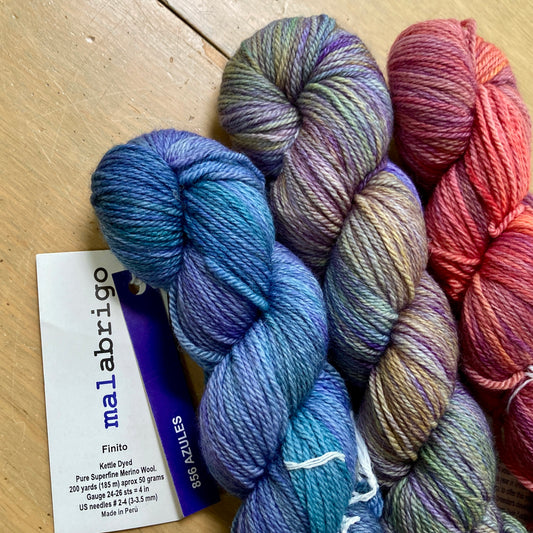 3 colorful skeins of Malabrigo Finito yarn lying on a wooden surface.