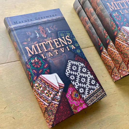 Four copies of Maruta Grasmane’s Mittens of Latvia book, stacked on a wooden surface.