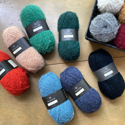 Colorful balls of Isager Bouclé yarn arranged on a wooden surface.