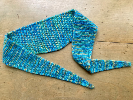 Variegated triangular turquoise neck scarf arranged on a wooden surface.