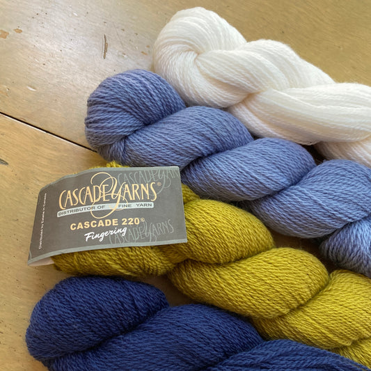 Four skeins of Cascade 220 Fingering yarn on a wooden table.