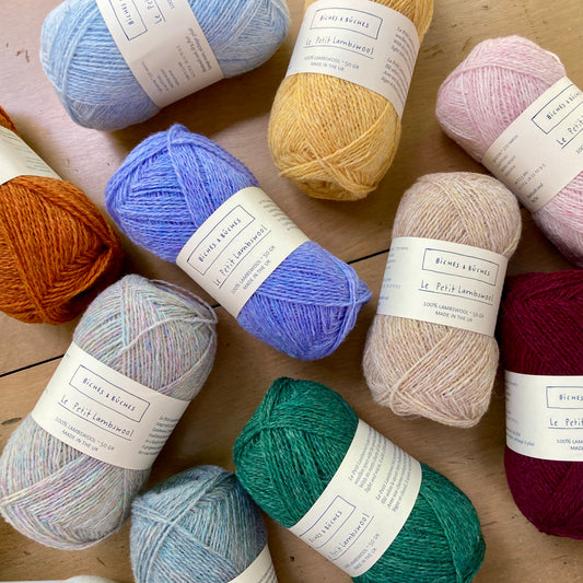 Colorful balls of Biches et Bûches Le Petit Lambswool yarn arranged on a wooden surface, on display at Hillsborough Yarn Shop