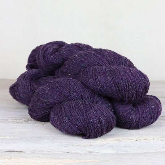 Three skeins of dark purple Fibre Co. Arranmore Light yarn.