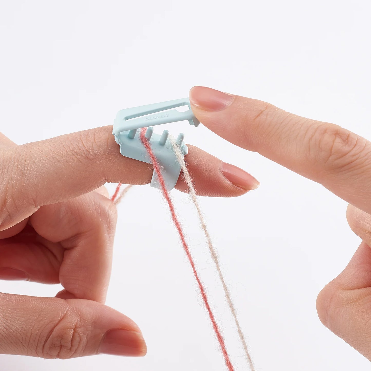 Image of the "open" Clover yarn guide attached to a knitter's left pointer finger, threading a red strand and a beige strand, illustrating how to attach or remove yarn.