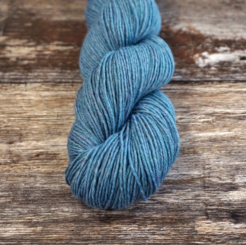 Blue skein of CoopKnits Socks Yeah! yarn on a wooden surface.