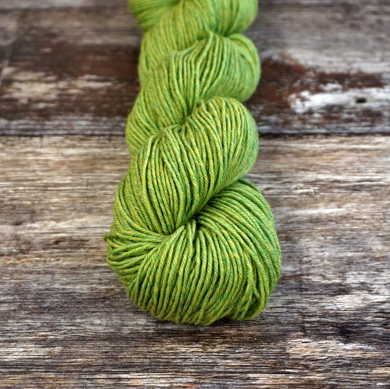 Bright green skein of CoopKnits Socks Yeah! yarn on a wooden surface.