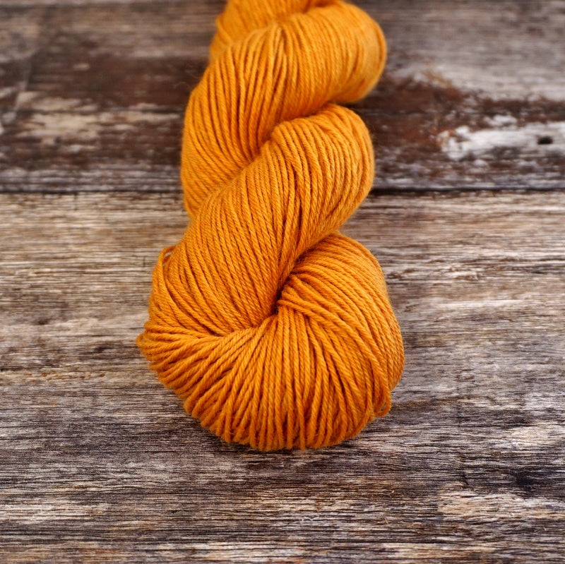 Golden orange skein of CoopKnits Socks Yeah! yarn on a wooden surface.