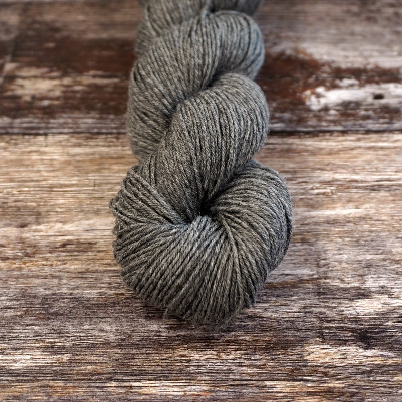 Heathered charcoal skein of CoopKnits Socks Yeah! yarn on a wooden surface.