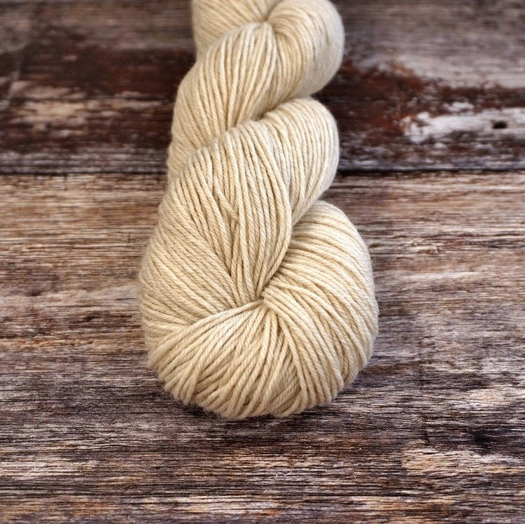 Beige skein of CoopKnits Socks Yeah! yarn on a wooden surface.