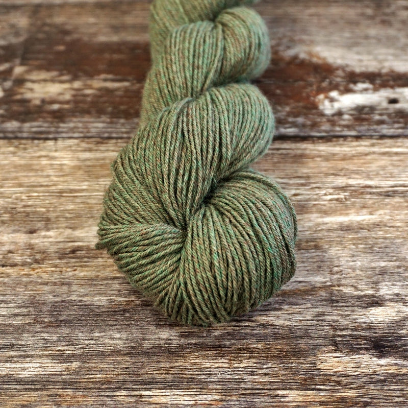 Moss green skein of CoopKnits Socks Yeah! yarn on a wooden surface.