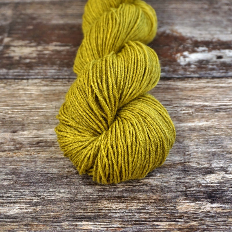 Chartreuse skein of CoopKnits Socks Yeah! yarn on a wooden surface.