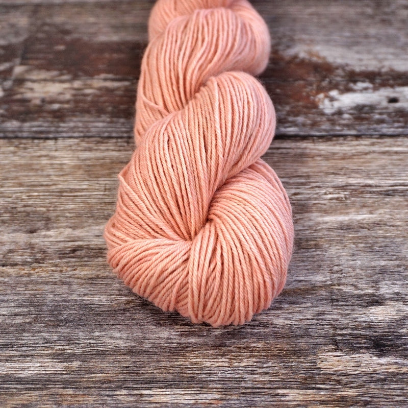 Light pink skein of CoopKnits Socks Yeah! yarn on a wooden surface.