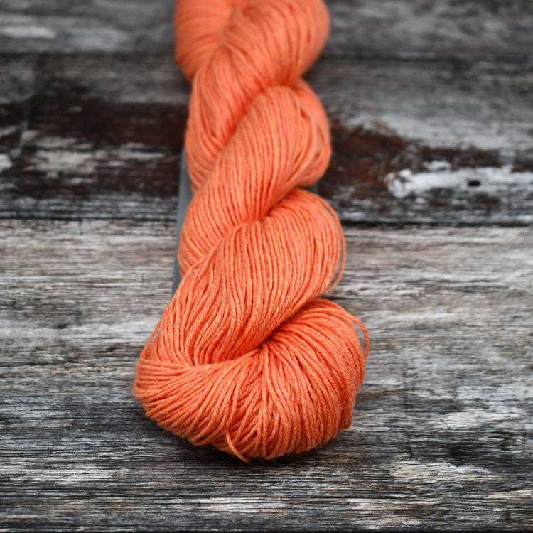 Lively orange skein of CoopKnits Socks Yeah! yarn on a wooden surface.