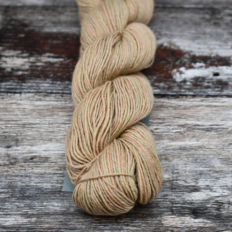 Beige with teal and peach skein of CoopKnits Socks Yeah! yarn on a wooden