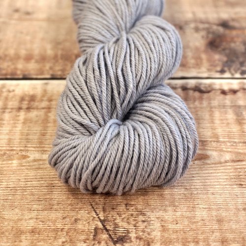 Light gray skein of CoopKnits Socks Yeah! DK yarn on a wooden surface.