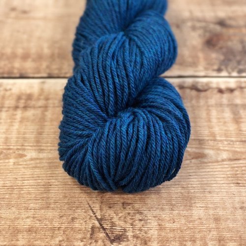 Dark teal blue skein of CoopKnits Socks Yeah! DK yarn on a wooden surface.