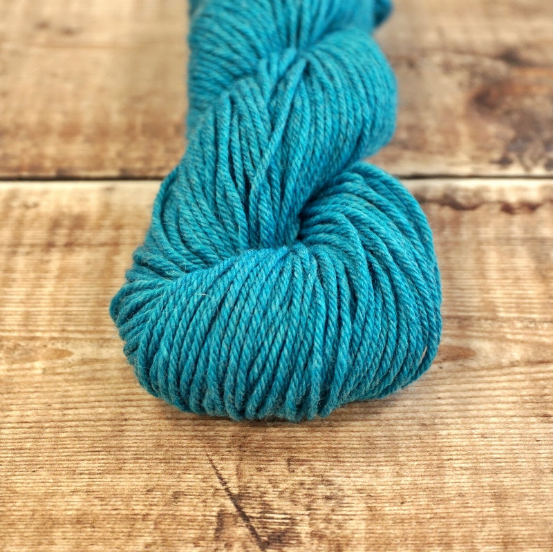 Bright teal skein of CoopKnits Socks Yeah! DK yarn on a wooden surface.