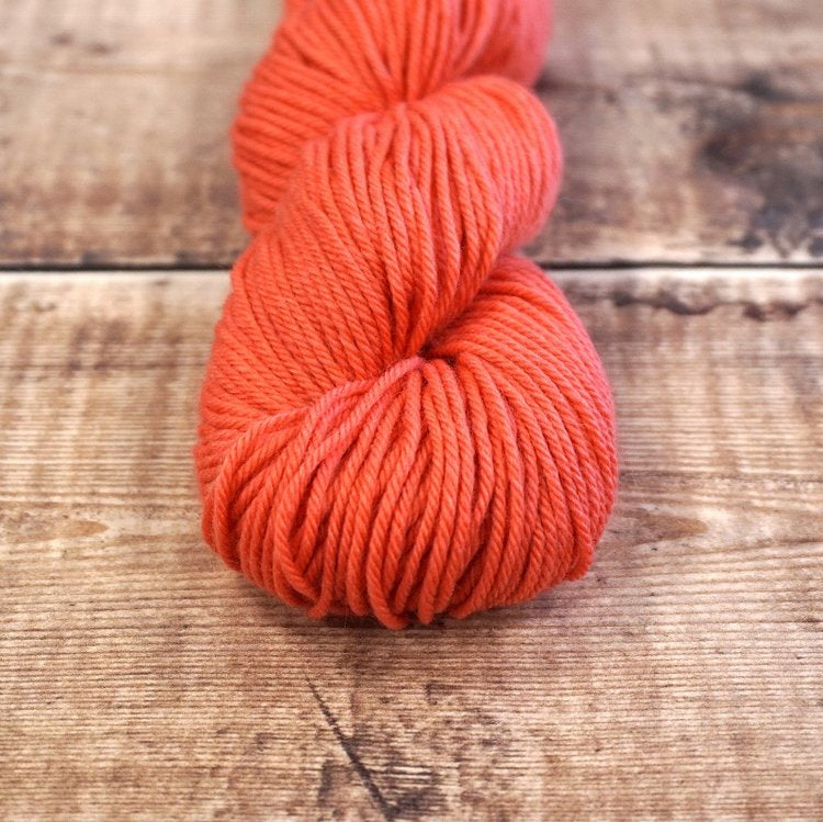 Coral skein of CoopKnits Socks Yeah! DK yarn on a wooden surface.