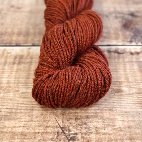 Rust red skein of CoopKnits Socks Yeah! DK yarn on a wooden surface.
