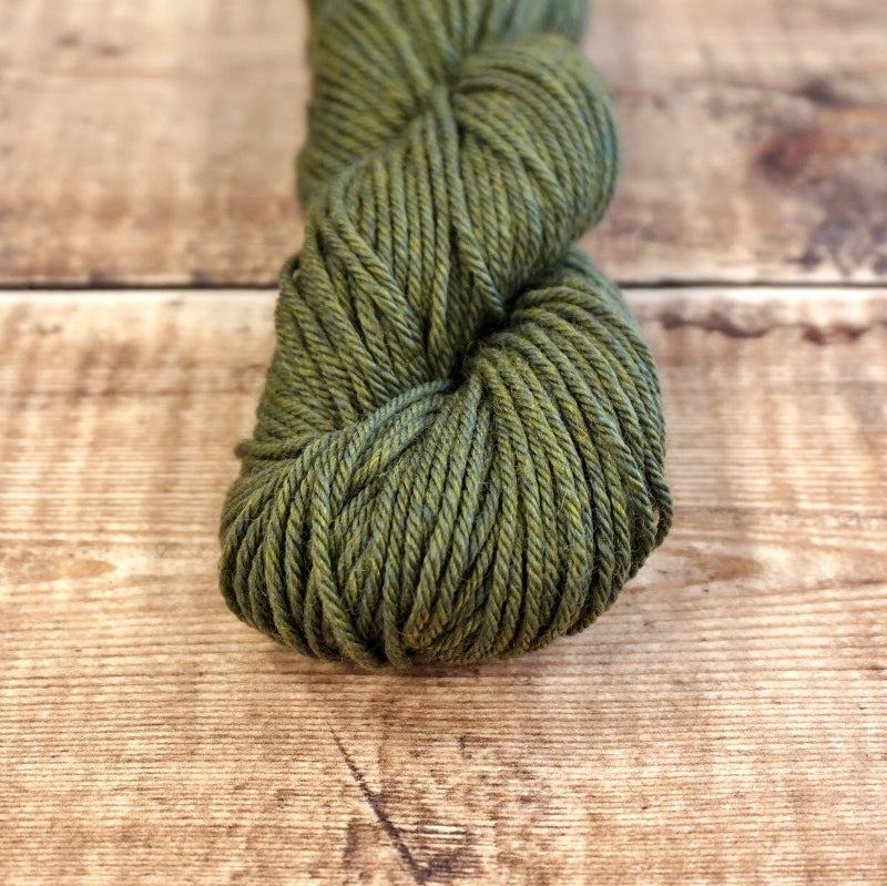 Algae green skein of CoopKnits Socks Yeah! DK yarn on a wooden surface.
