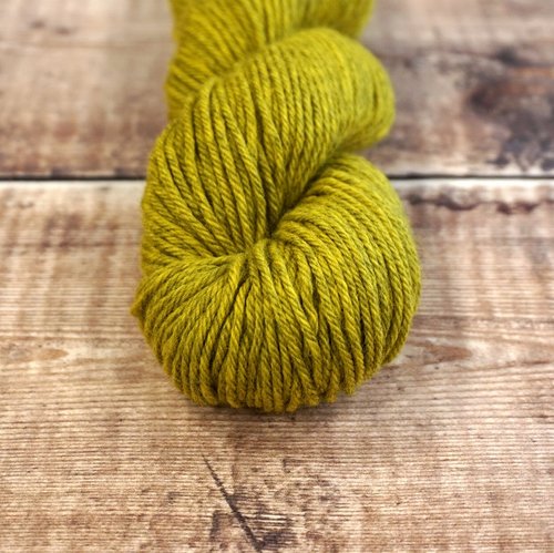 Chartreuse skein of CoopKnits Socks Yeah! DK yarn on a wooden surface.