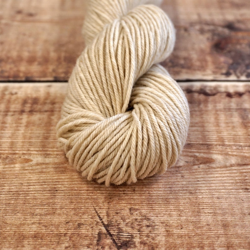 Wheat colored skein of CoopKnits Socks Yeah! DK yarn on a wooden surface.