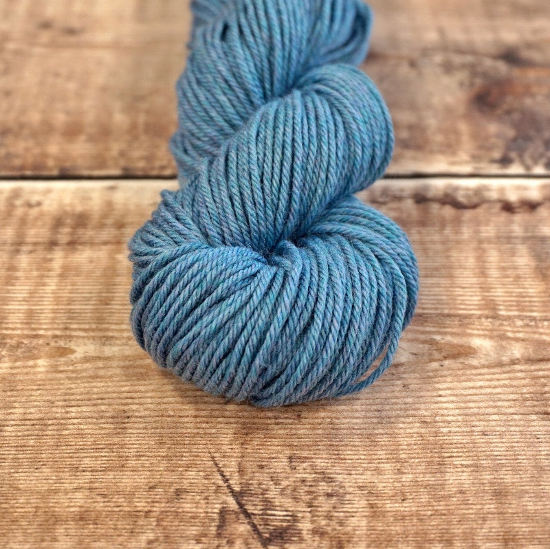 Sea blue skein of CoopKnits Socks Yeah! DK yarn on a wooden surface.