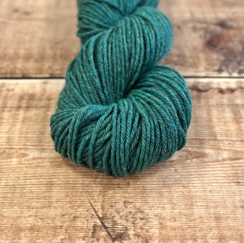 Sea green skein of CoopKnits Socks Yeah! DK yarn on a wooden surface.