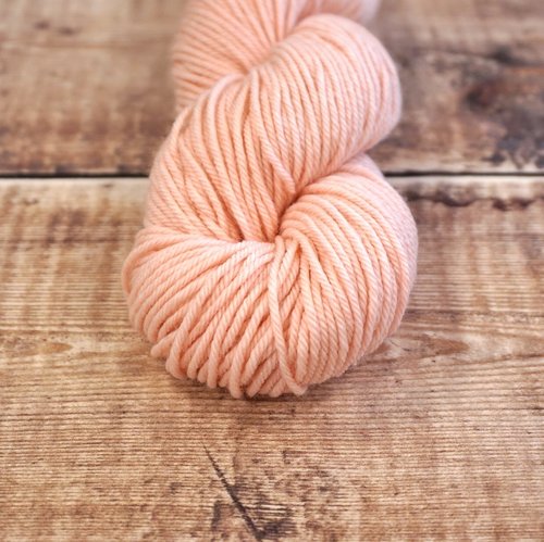 Light pink skein of CoopKnits Socks Yeah! DK yarn on a wooden surface.