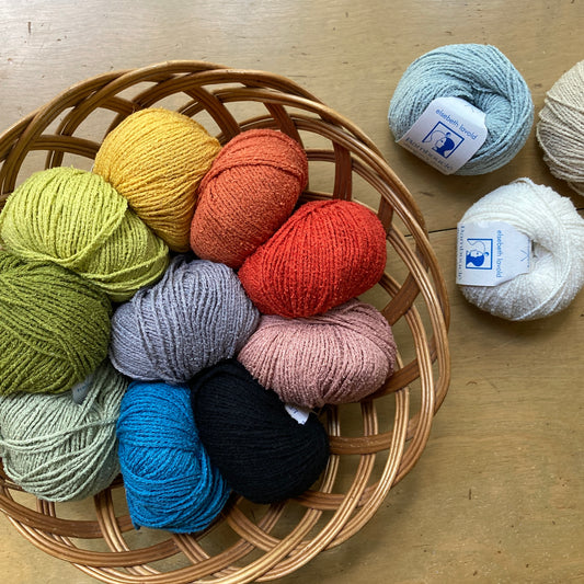 Colorful balls of Elsebeth Lavold Bambouclé in a basket on a wooden surface.