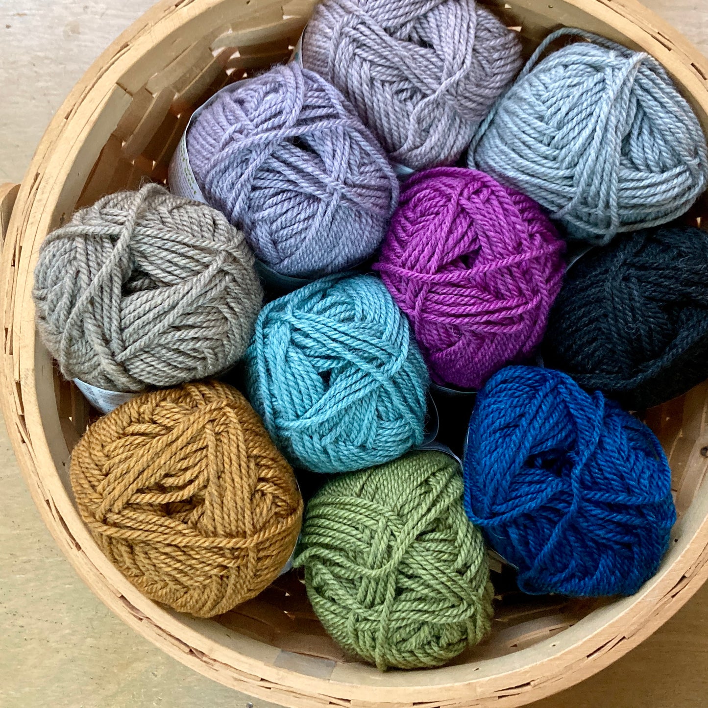 Colorful basket full of Ewe Ewe Heather’s Heathers yarn on a wooden surface.
