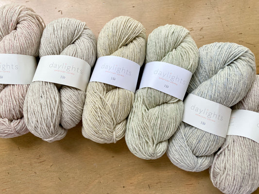 Row of light-colored Harrisville daylights yarn skeins on a wooden surface
