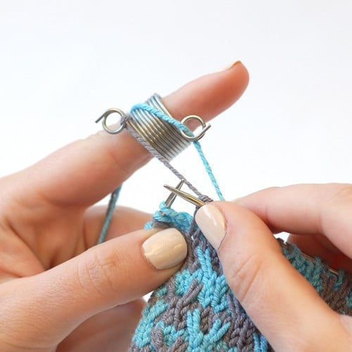 Close up on two hands knitting blue and gray colorwork using an Addi knitting thimble.