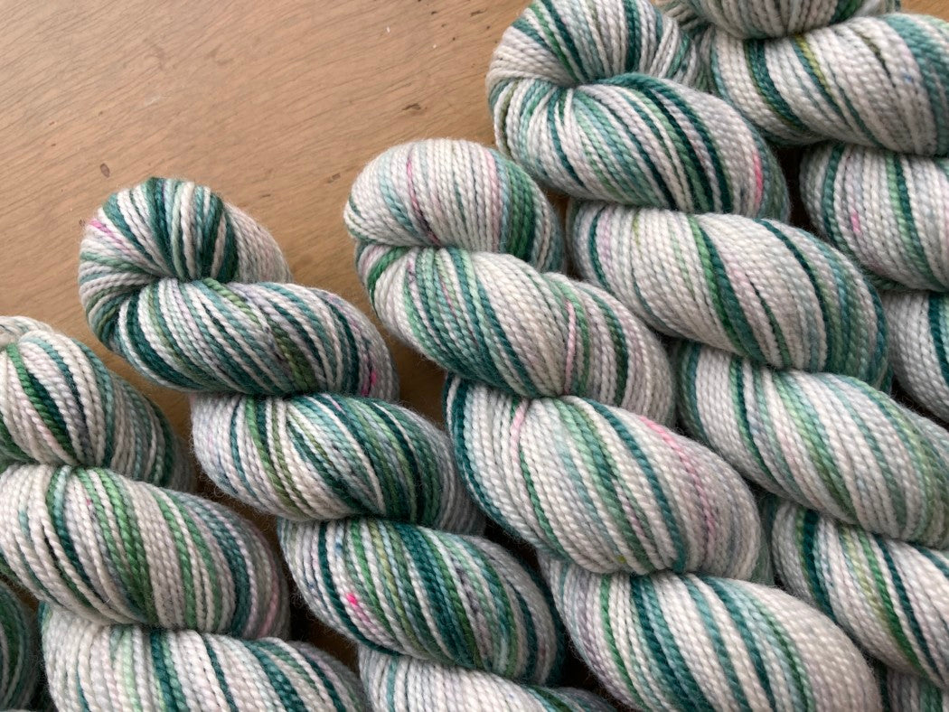 Cream and teal variegated skeins of Koigu KPPPM yarn arranged on a wooden surface.