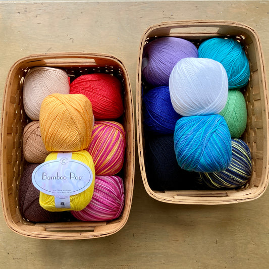 Two rectangular baskets on a wooden surface, each filled with colorful balls of Universal Bamboo Pop yarn.