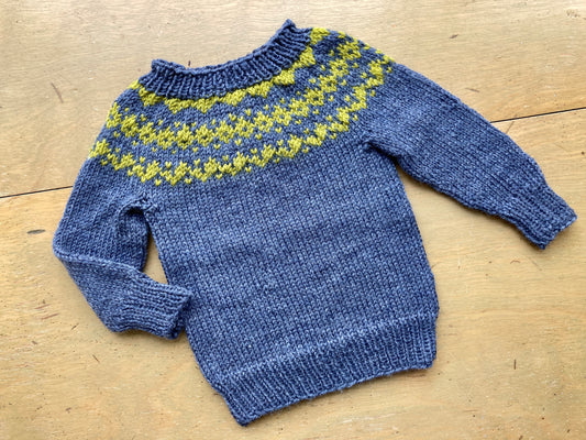 Gray and green colorwork yoke baby sweater lying on a wooden surface.
