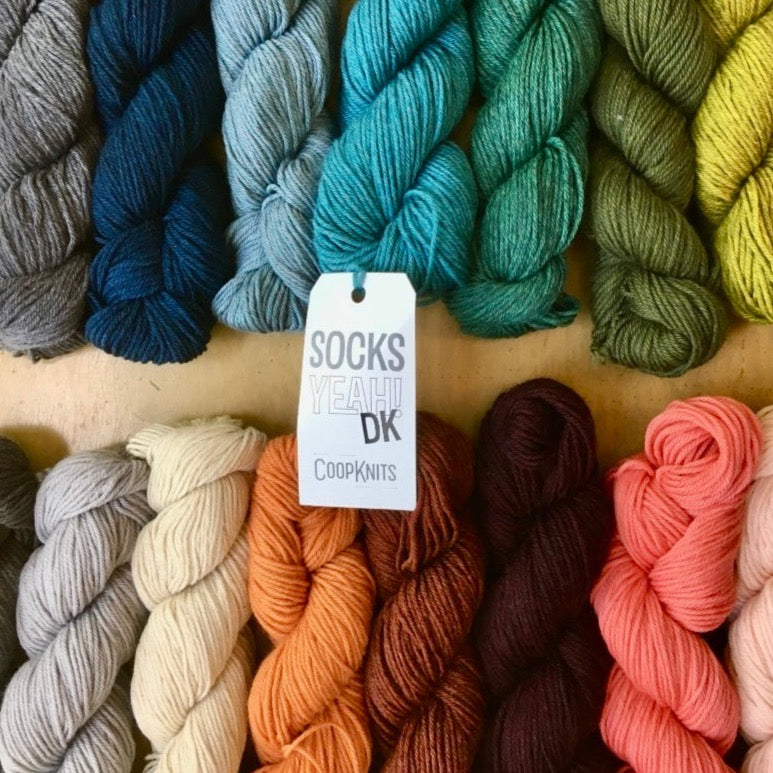 Colorful skeins of CoopKnits Socks Yeah! DK arranged on a wooden surface.