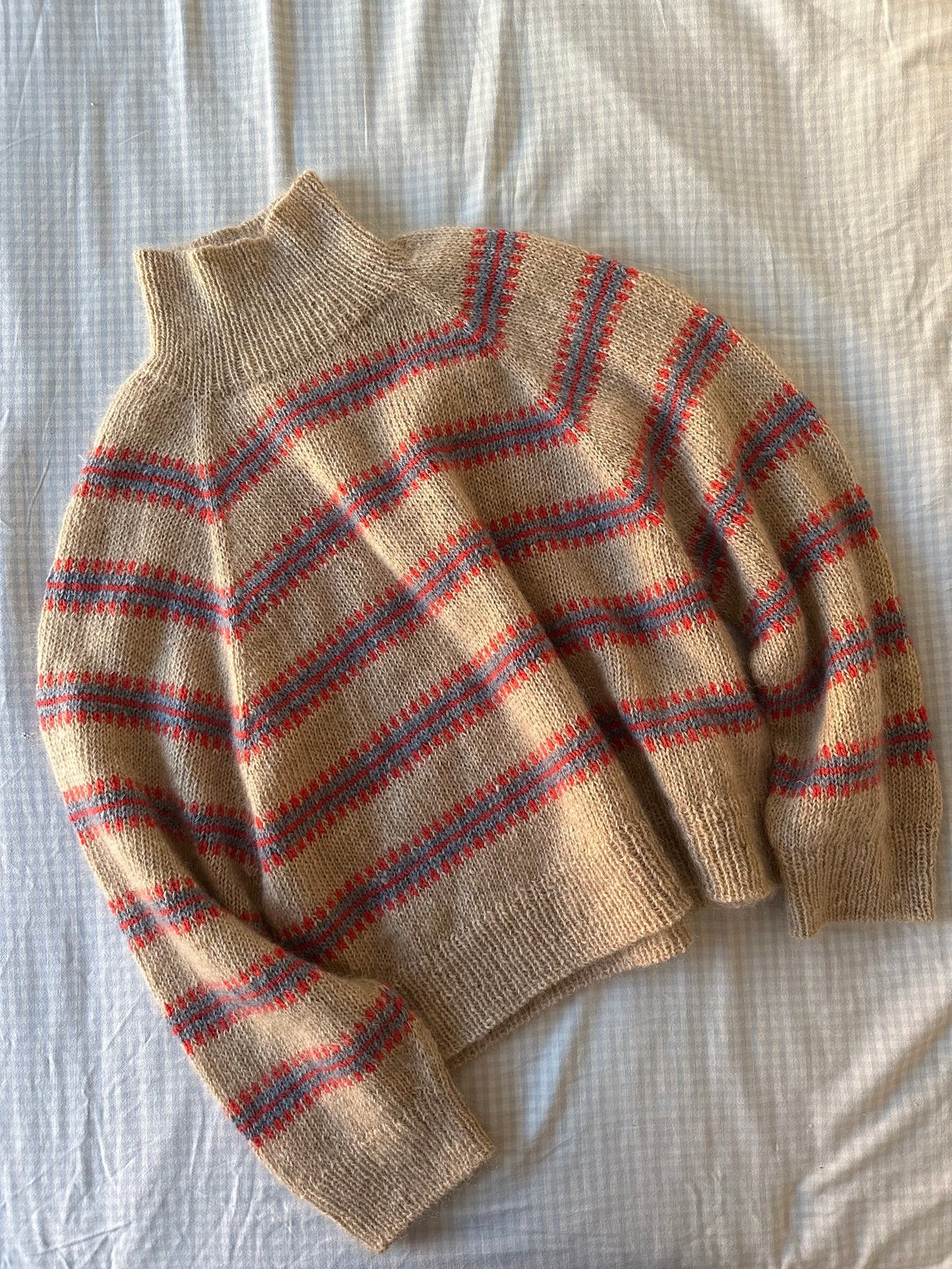 Norma sweater laying flat on a cream colored bed sheet