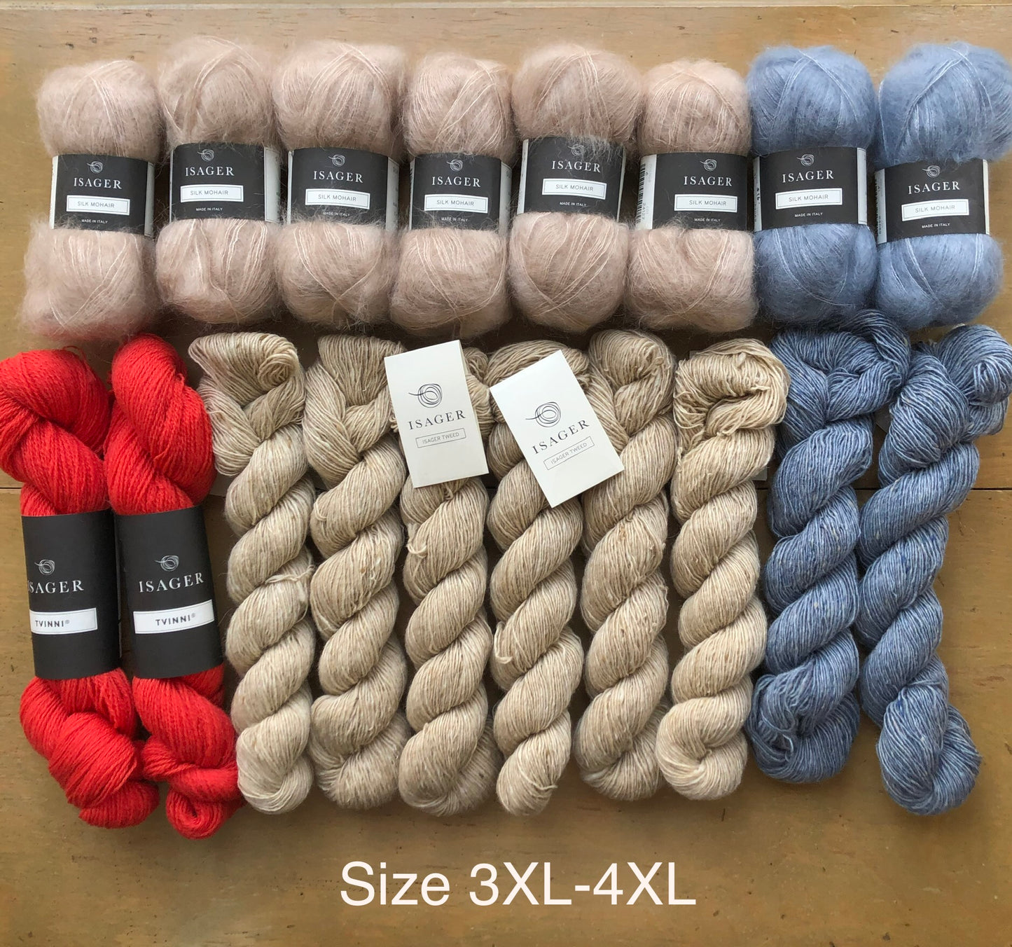 Contents of 3XL-4XL Norma sweater kit on wooden table. Clockwise from left: 6 balls Isager Silk Mohair in beige, 2 balls Isager Silk Mohair light blue, 2 skeins Isager Tweed in Topaz, 6 skeins Isager Tweed in Sand, and 2 skeins Isager Tvinni in red.